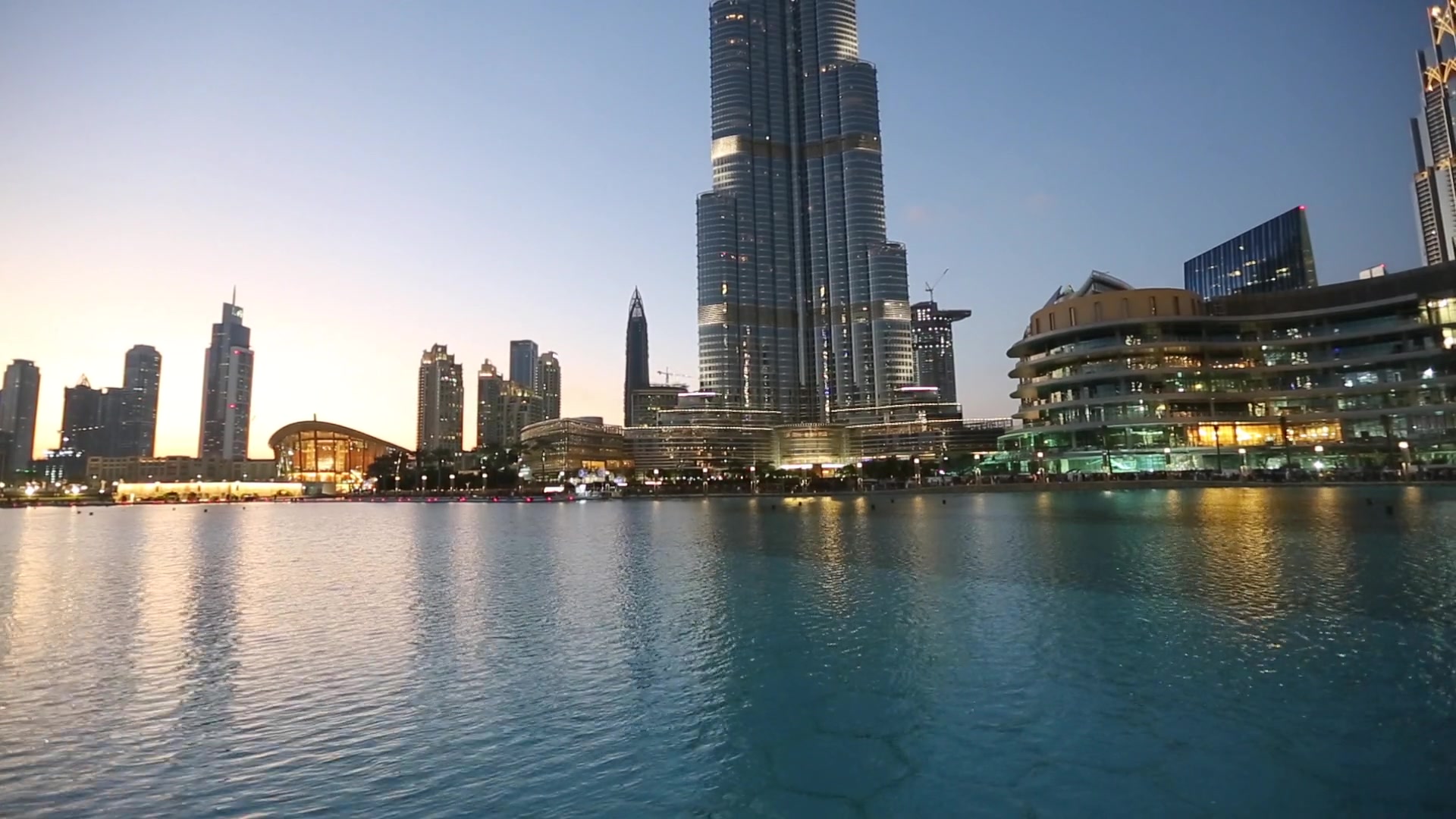 Real view across the Dubai Fountain lake toward Burj Khalifa and Dubai Mall at dusk